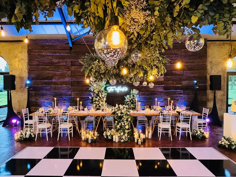 A candlelit head table and chequered dancefloor under hanging greenery and chandeliers