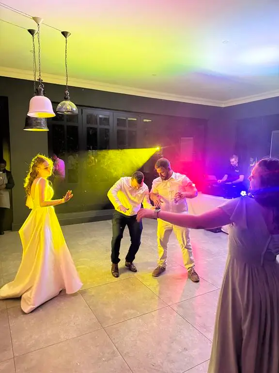 A bride in white dancing under a yellow lighting beam at her wedding