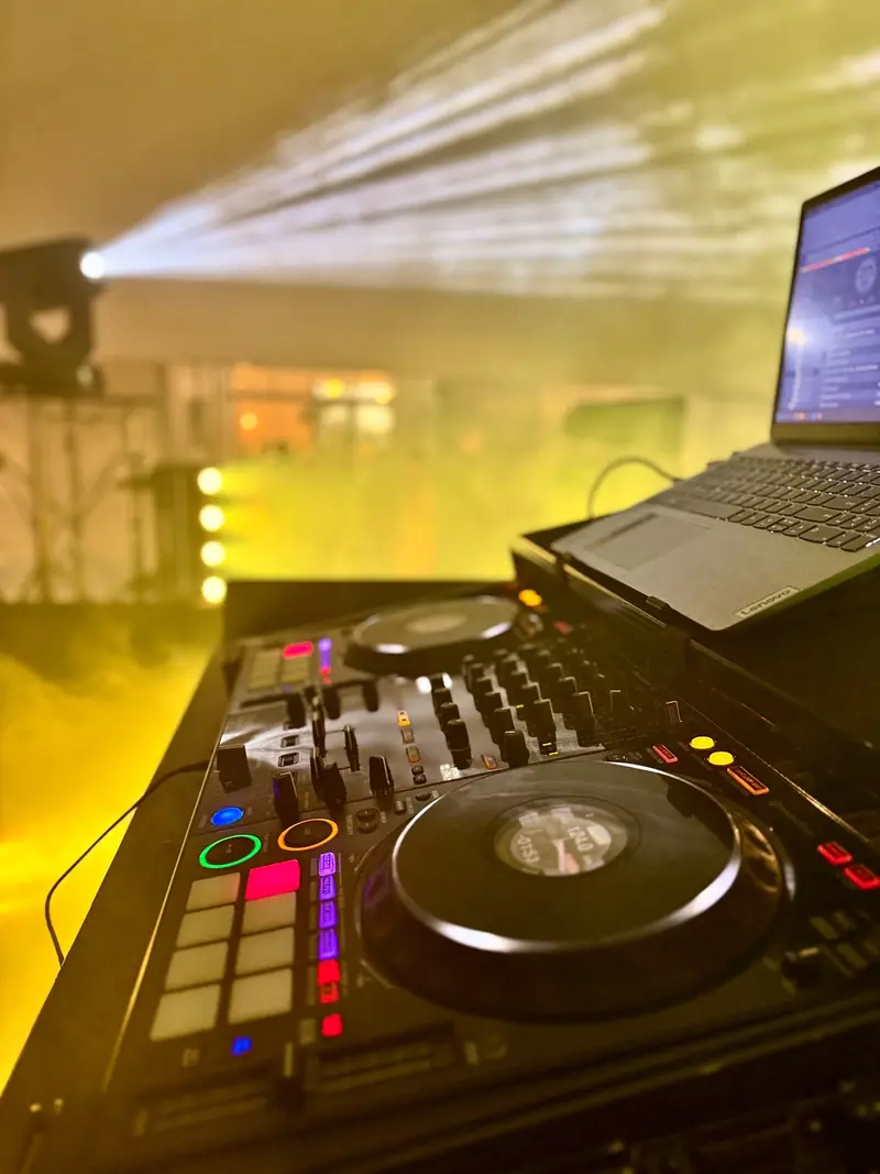 DJ controller and laptop in the booth with light beams cutting through haze