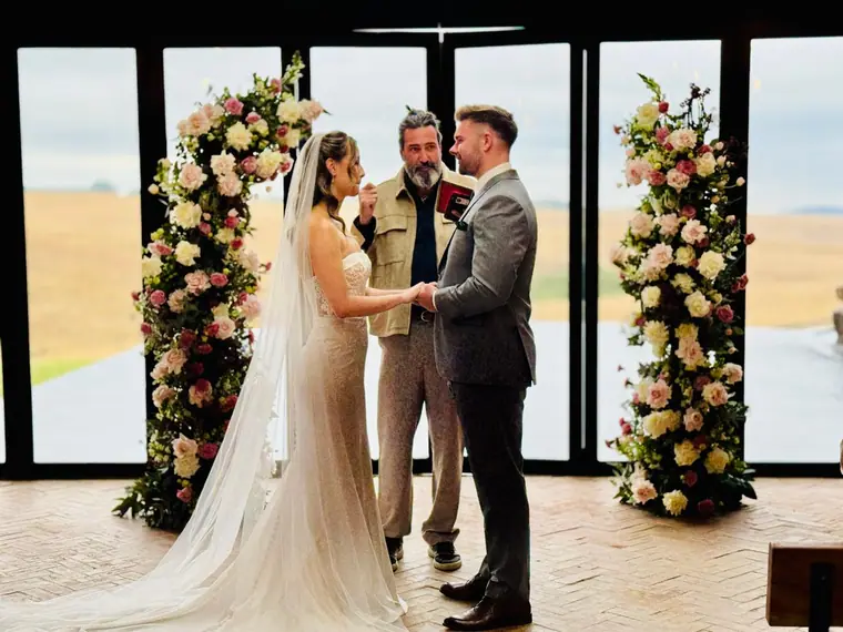 Bride and groom under a floral arch at sunset